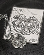 A 990 fine silver tiger head pendant alongside an exquisite hand-painted card, crafted by Dzoo for Rainbow Tears.