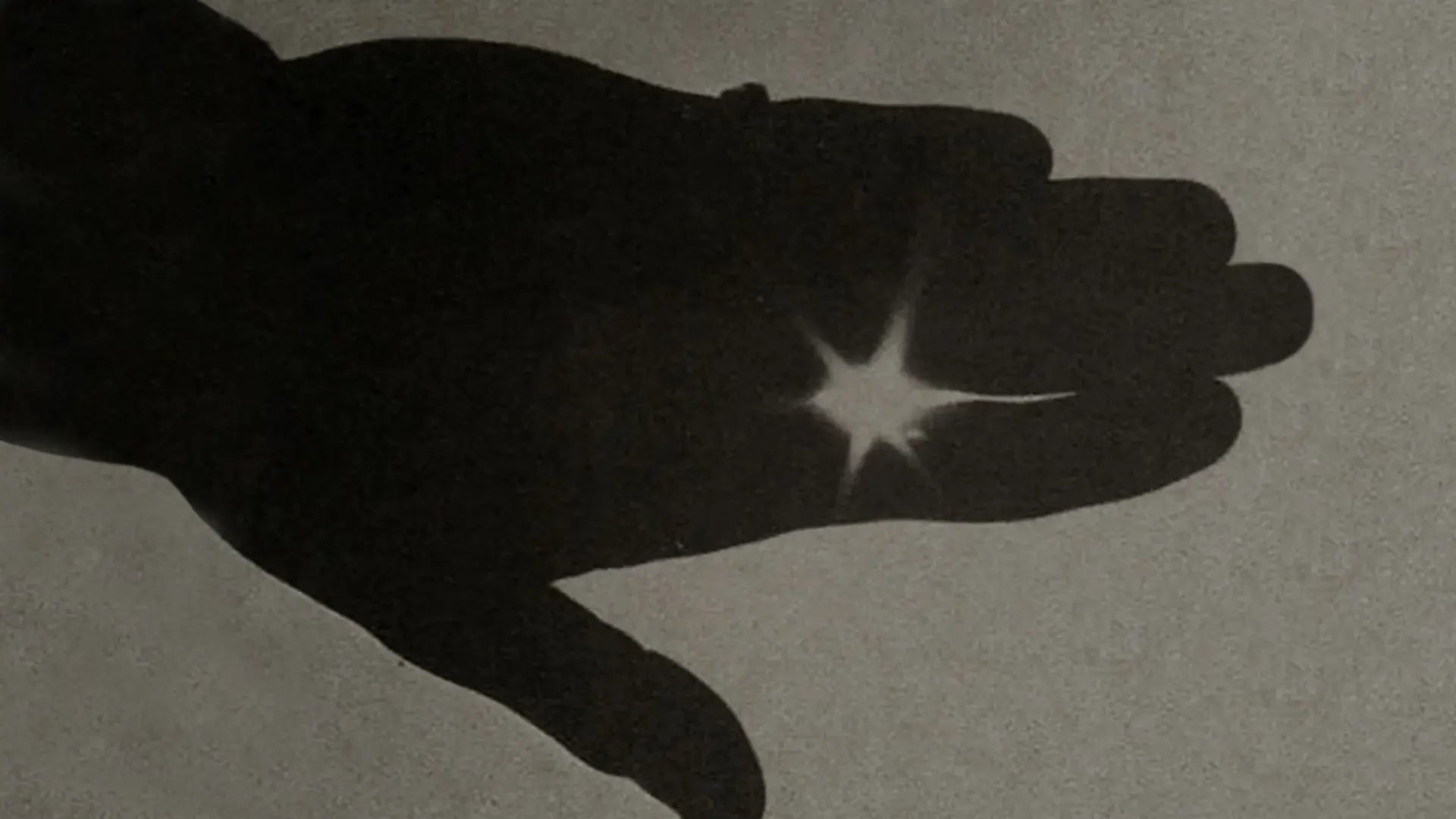A minimalist grayscale silhouette of a hand with light shining through fingers for Rainbow Tears.