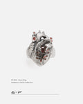 Silver stitched broken heart ring with a red zircon stone on a white background, by Dzoo, available at Rainbow Tears.