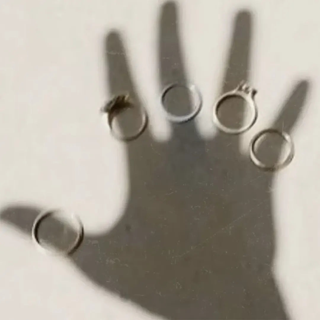 Shadow of an open hand wearing five unique designer rings, capturing Rainbow Tears' aesthetic of emotion and light.