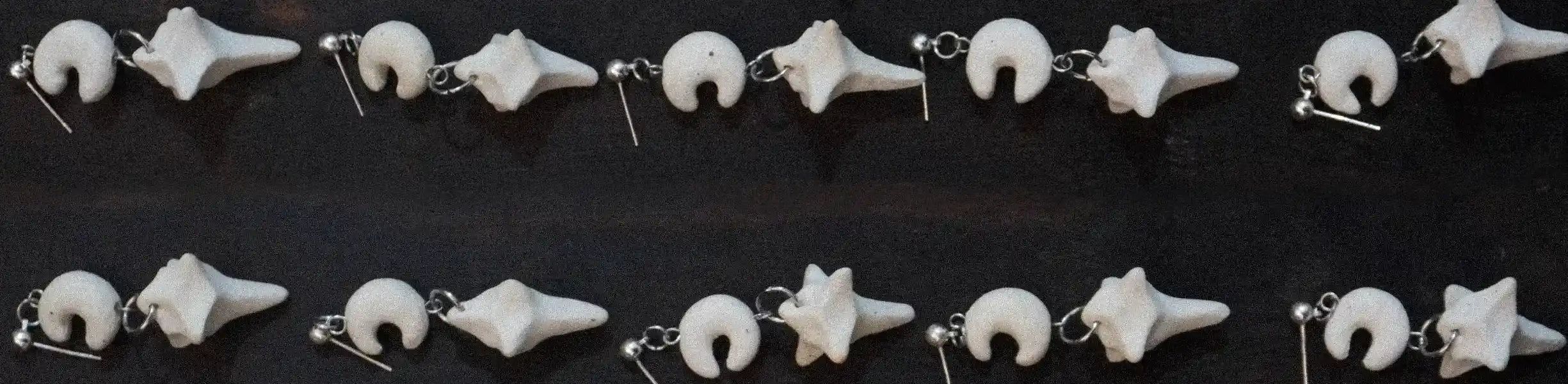 Five pairs of white ceramic star and moon earrings arranged in two orderly rows, reflecting a celestial design.