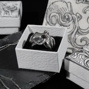 A silver octopus ring displayed inside a hand-drawn octopus jewelry box with a fabric pouch in the background.