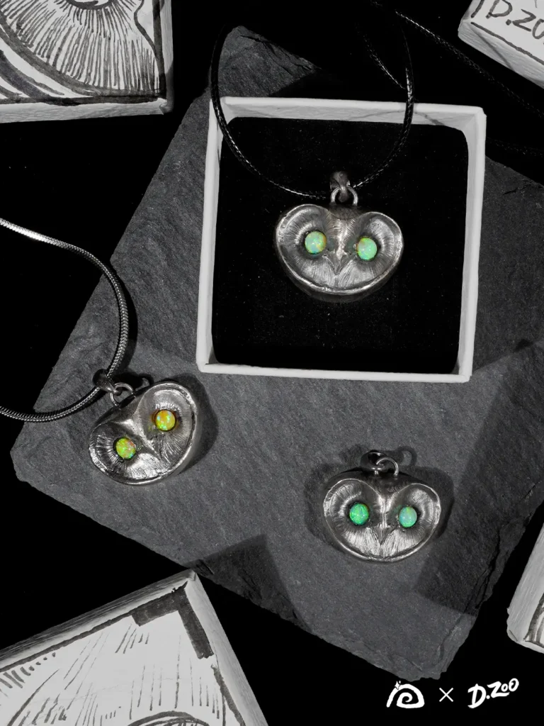 Three owl necklaces with opal eyes, including one yellow-tone opal and two blue-tone opals, displayed with a hand-drawn jewelry box.