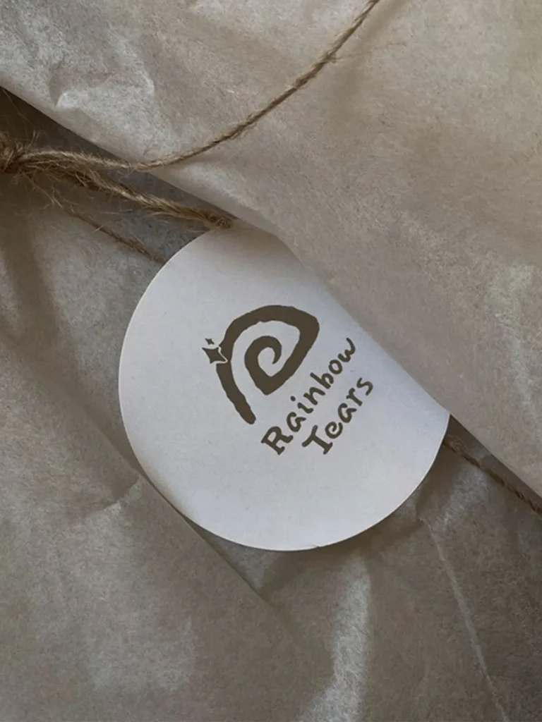 White circular Rainbow Tears logo label placed loosely on brown wrapping paper for brand presentation.