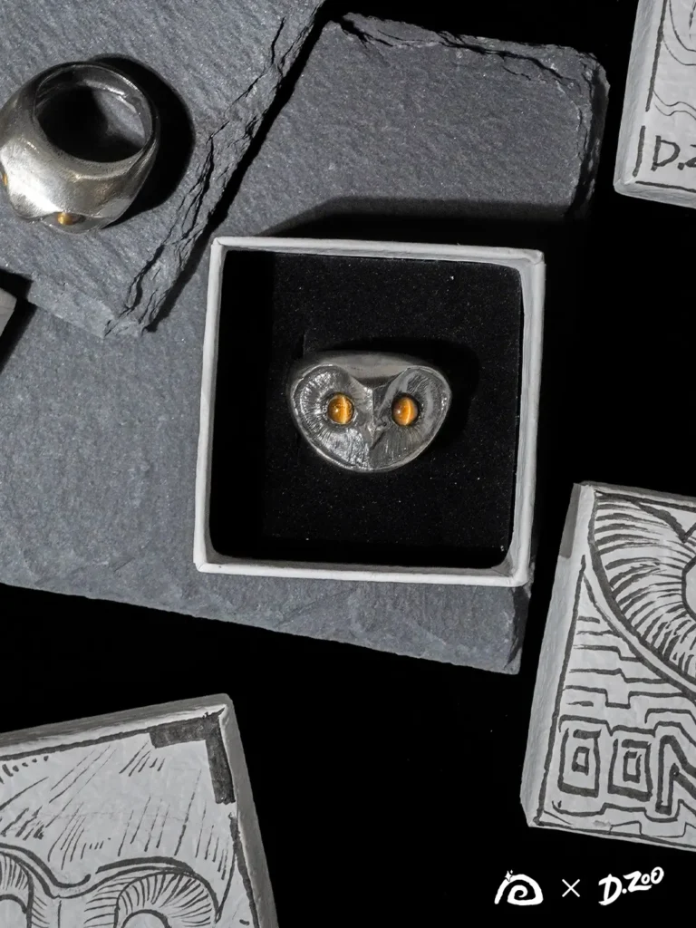 Two sterling silver owl rings displayed in a jewelry box and on a stone slab