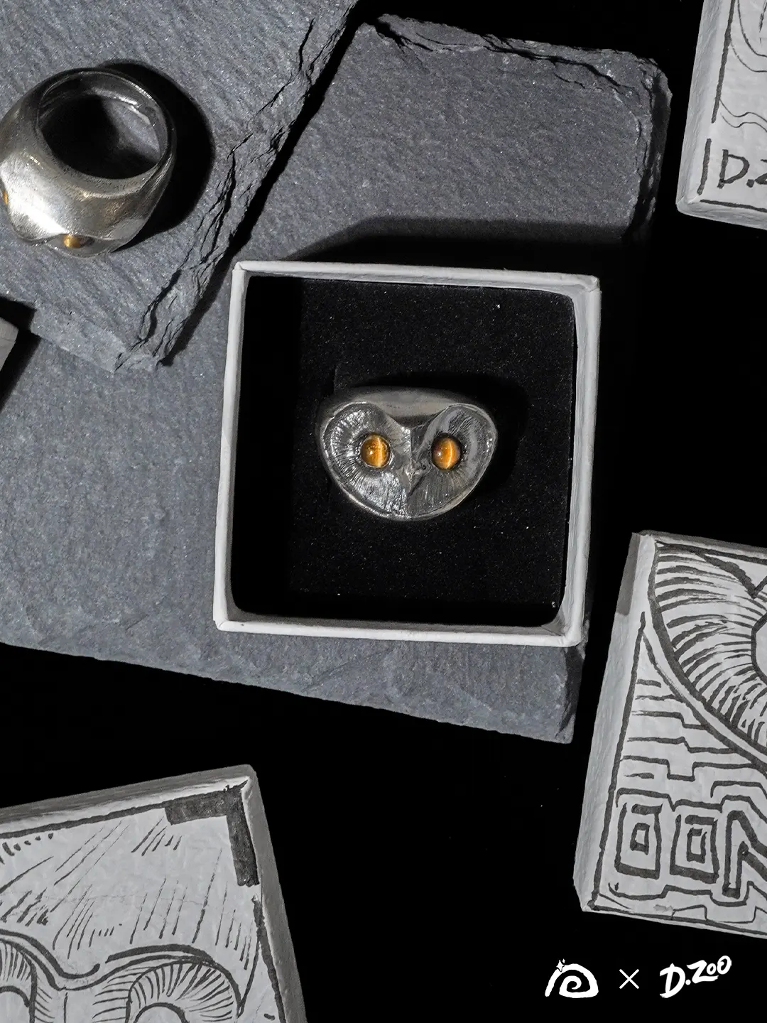 Two sterling silver owl rings displayed in a jewelry box and on a stone slab