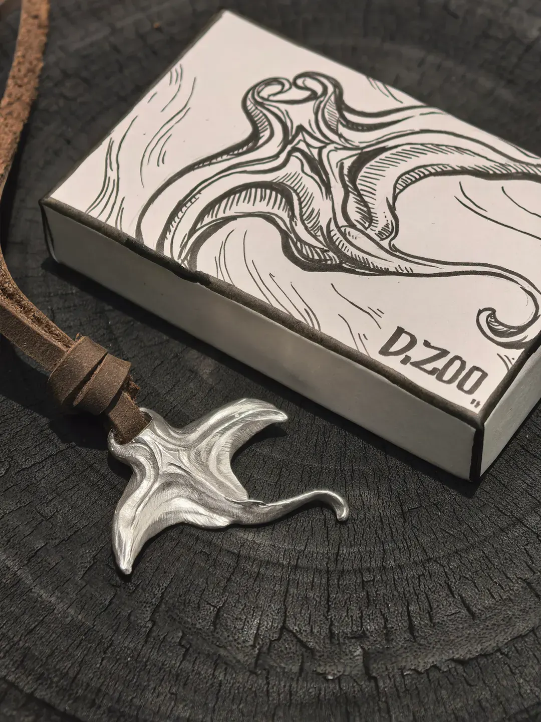 A silver sea-inspired pendant tied with a leather cord beside a hand-painted jewelry box