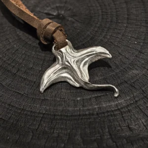 Manta ray necklace with leather cord displayed on a black wood background
