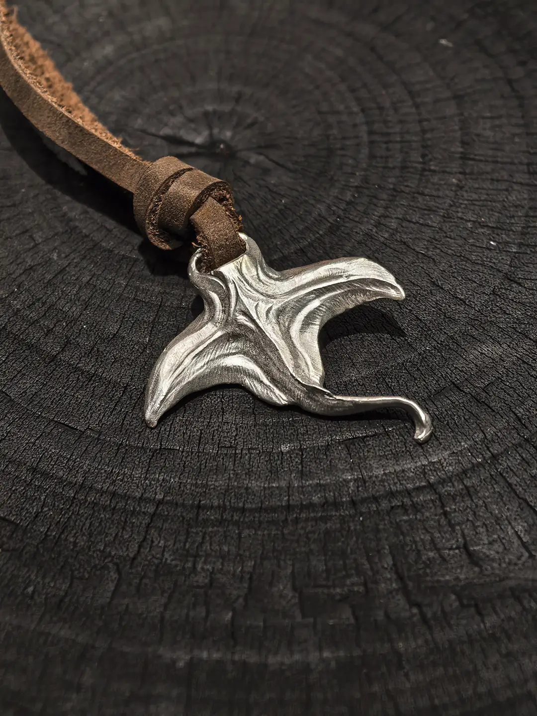 Manta ray necklace with leather cord displayed on a black wood background