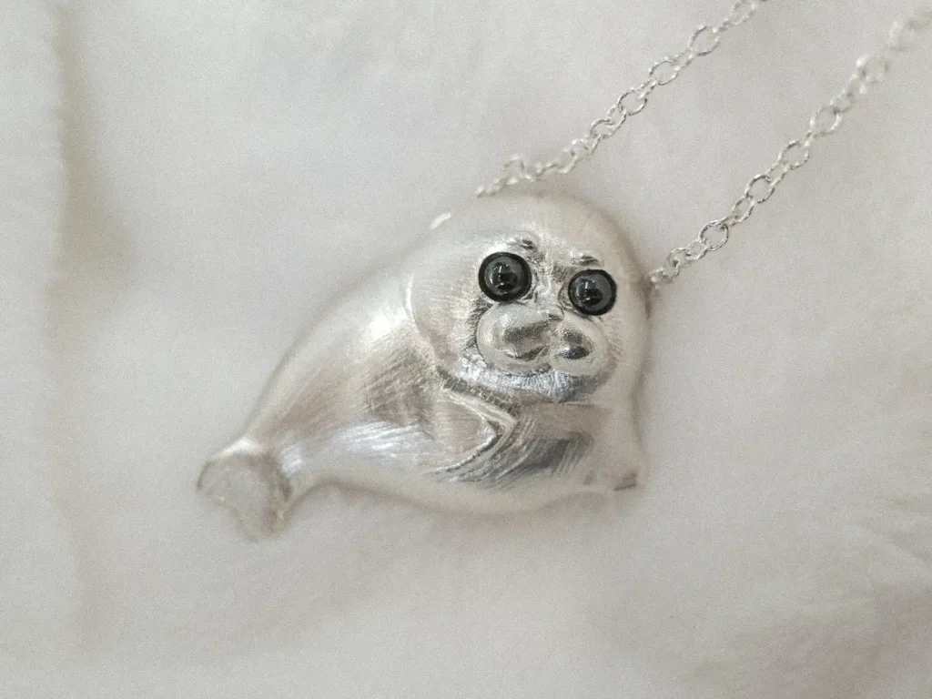 A cute seal animal jewelry piece is placed on a white blanket