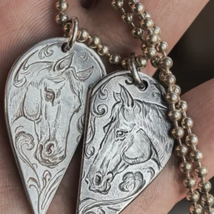 A pair of 990 fine silver half-heart pendants being held in hands, featuring custom hand-engraved horse motifs that form a complete heart when joined together.