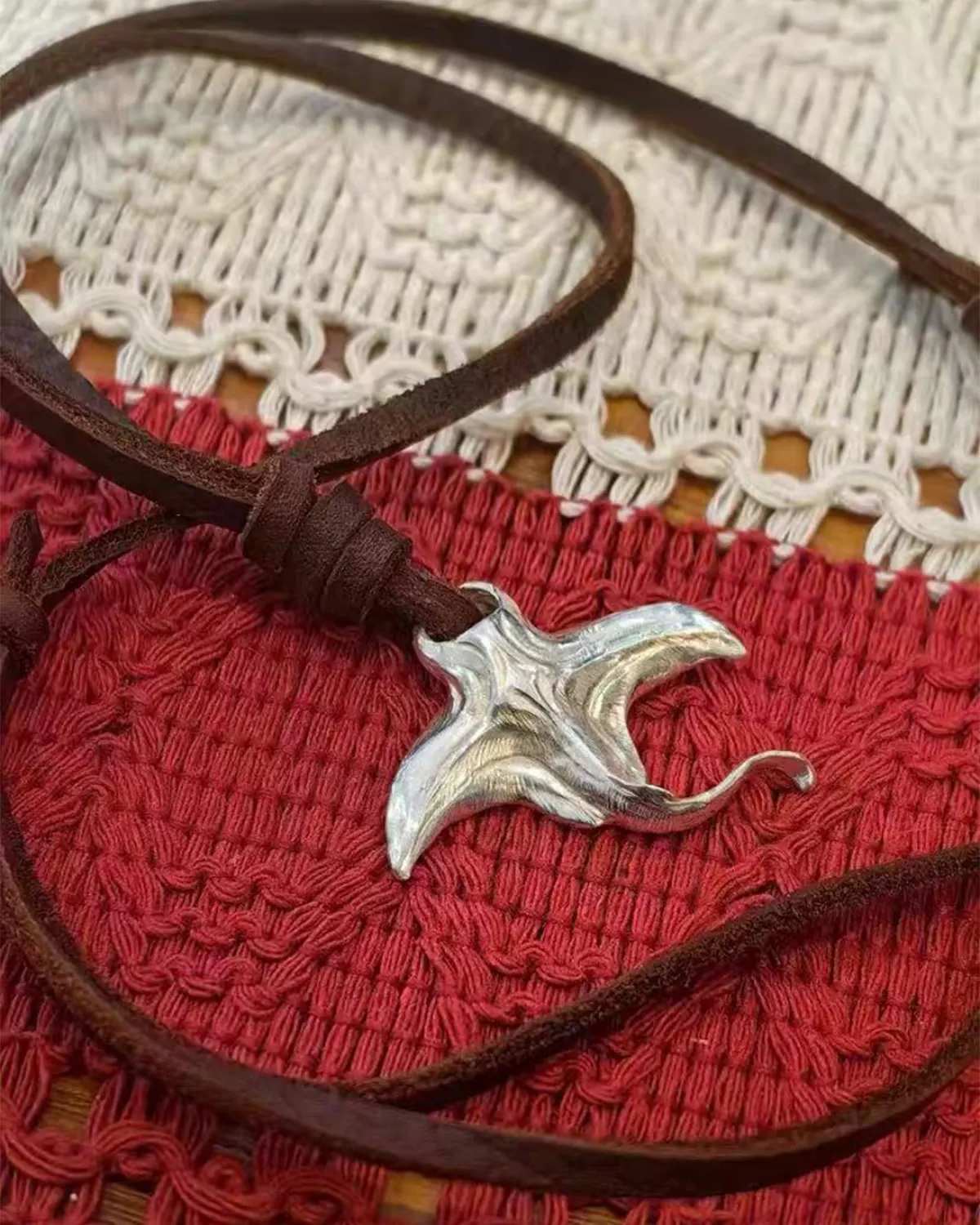 A handcrafted 925 sterling silver manta ray pendant on a black leather cord, displayed on a red and white patterned blanket.