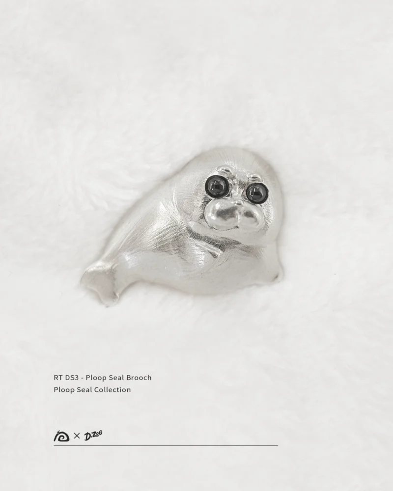 Front view of the pure silver Ploop seal brooch placed on white velvet