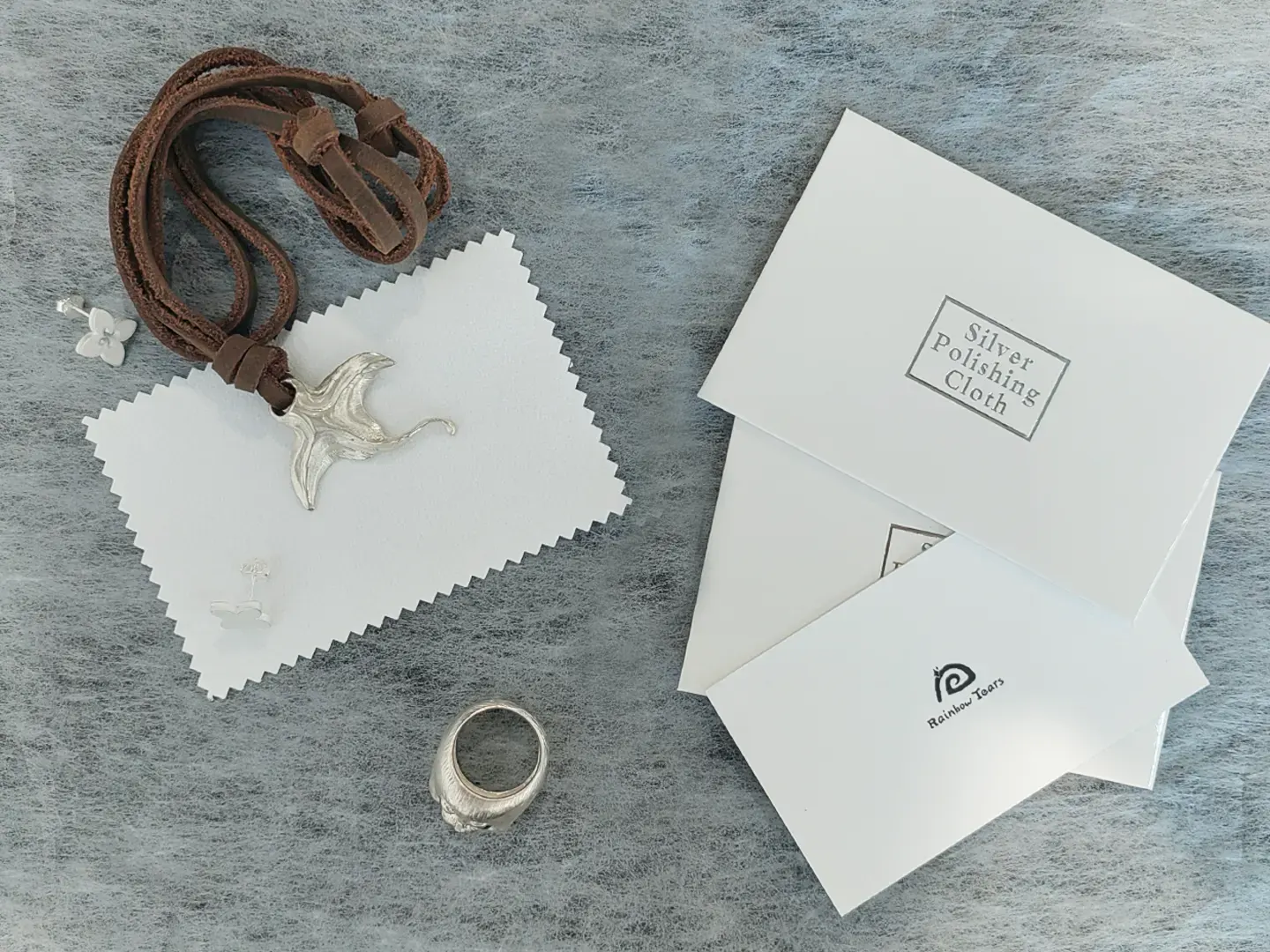 A manta ray pendant and seal ring in 925 sterling silver placed next to a jewelry polishing cloth for a silver jewelry care guide.