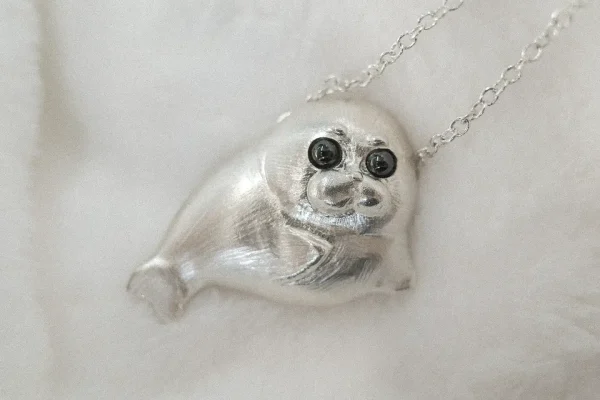 A cute seal animal jewelry piece is placed on a white blanket